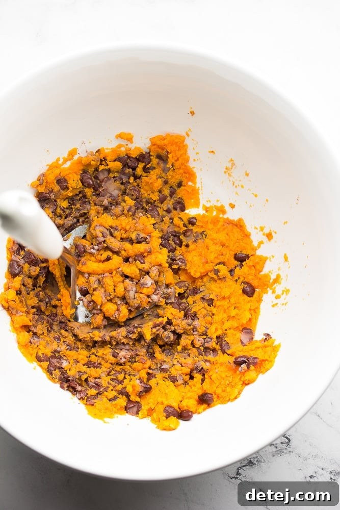 Bowl with cooked sweet potato and black beans being mashed together, showing a rich orange and black mixture.