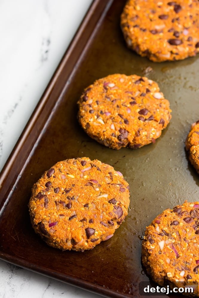 Uncooked sweet potato black bean burger patties arranged on a greased baking pan, ready for the oven.