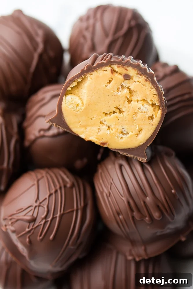 Close up of a vegan chocolate peanut butter ball cut in half, showcasing its creamy peanut butter and crispy Rice Krispies interior and smooth chocolate coating.