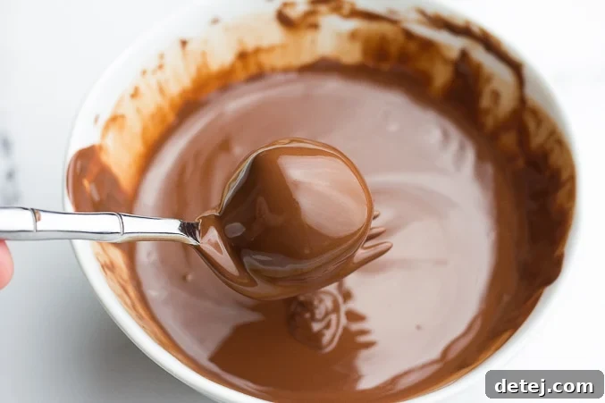 A vegan peanut butter ball being carefully dipped into a bowl of rich, melted vegan chocolate using a fork.