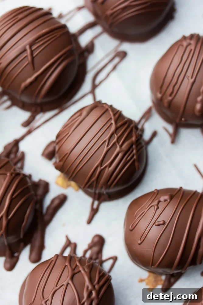 Close up view of several perfectly formed vegan chocolate peanut butter balls, some with a decorative chocolate drizzle, resting on parchment paper.