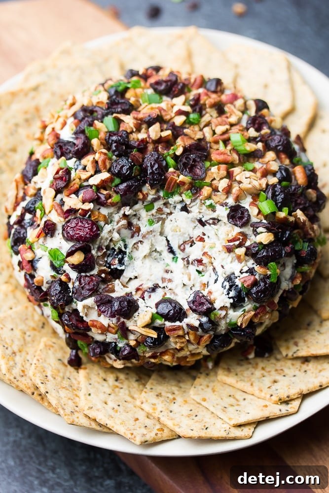 A delectable vegan cranberry pecan cheese ball with a section scooped out, revealing its creamy white interior, ready to be enjoyed.