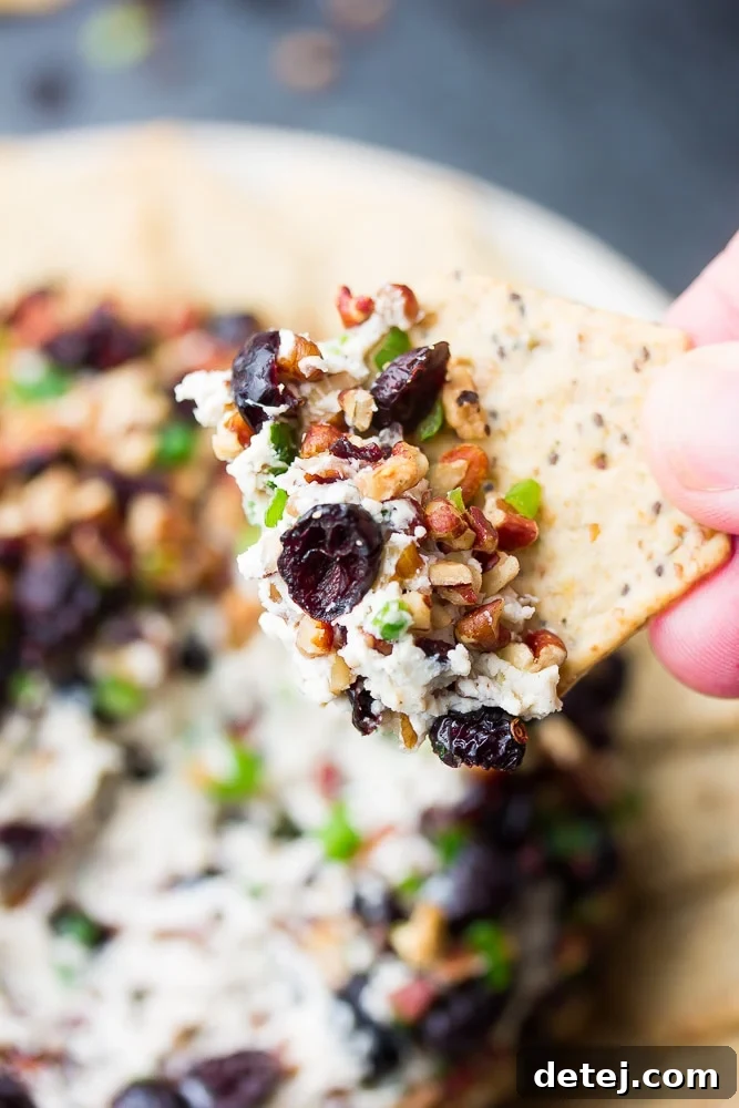 A crunchy cracker adorned with a generous dollop of creamy vegan cranberry pecan cheese ball, inviting a delicious bite.
