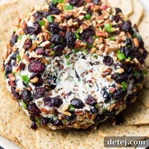 A delectable vegan cranberry pecan cheese ball with a section scooped out, revealing its creamy white interior, ready to be enjoyed.