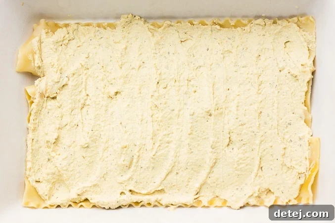 A smooth layer of creamy vegan ricotta is spread over the lasagna noodles, ready for the next layer of the Vegan White Lasagna.