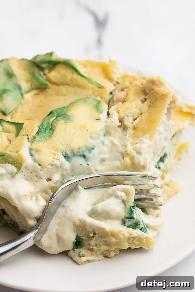 A fork cuts into a serving of Vegan White Lasagna, lifting a delicious bite filled with creamy layers and spinach.