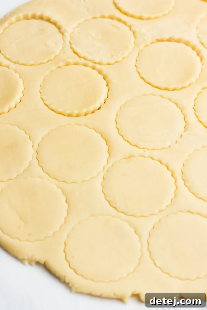 Various shortbread cookies being cut out from rolled dough using a round cookie cutter.