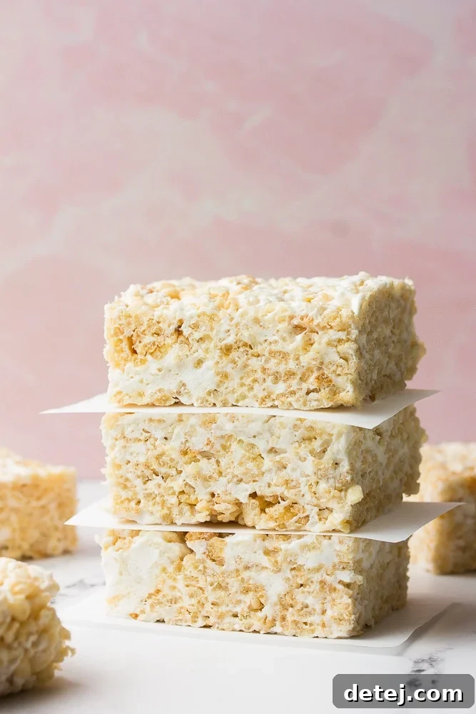 Stack of perfectly golden Vegan Rice Krispie Treats on a vibrant pink background, showcasing their irresistible chewiness.