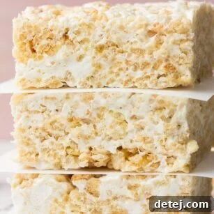 Close-up shot of perfectly gooey Vegan Rice Krispie Treats, stacked and ready to enjoy, with a soft pink background.