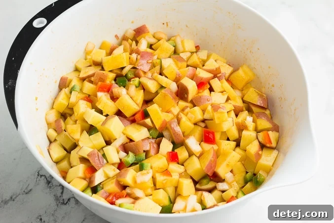 A bowl filled with freshly diced red potatoes, chopped onions, and colorful red and green bell peppers, tossed with olive oil and spices, ready for roasting.