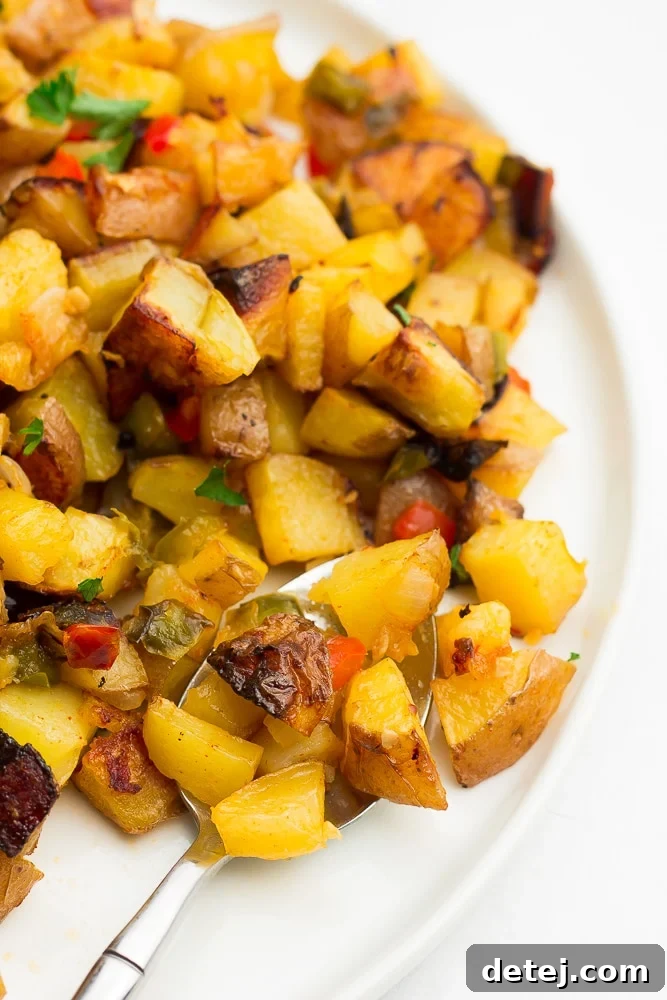 A close-up shot of cooked, diced breakfast potatoes on a plate, showing their golden brown, crispy texture, garnished with a sprinkle of fresh green herbs.
