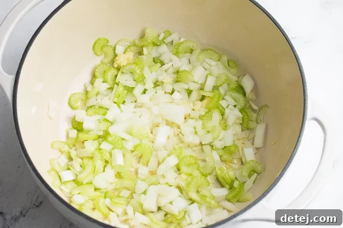 Close-up of chopped celery and onions gently sizzling in olive oil within a large pot, beginning the aromatic base of the soup.