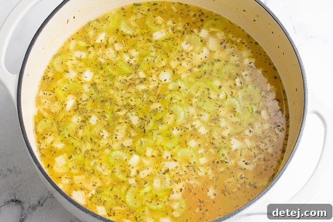 A pot filled with savory vegan broth, vibrant carrots, and plant-based 'chicken' pieces, simmering to perfection, forming the rich base of the noodle soup.