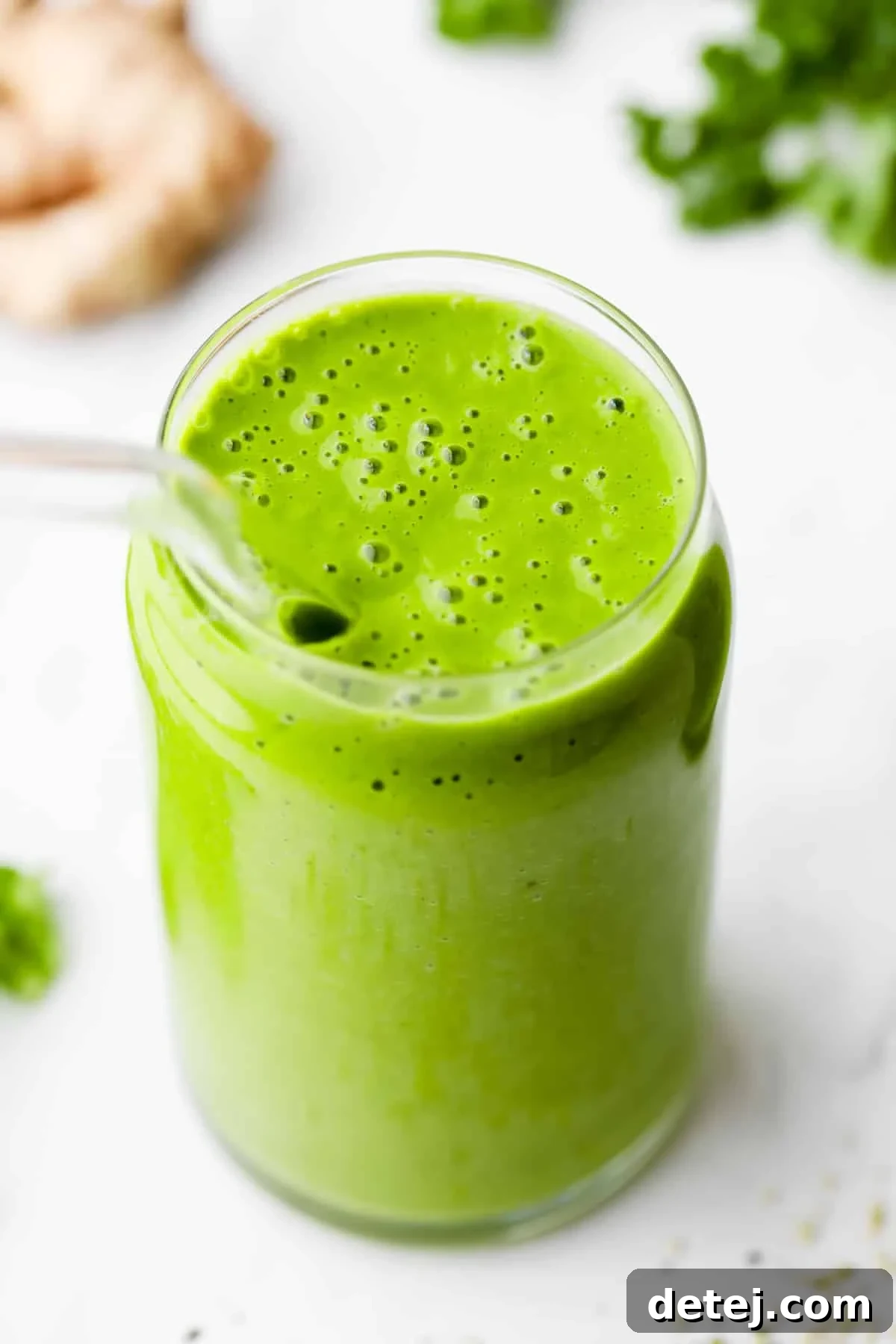 A vibrant green kale smoothie in a glass cup with a straw, accompanied by fresh ginger and kale on a wooden board, showcasing its natural ingredients.