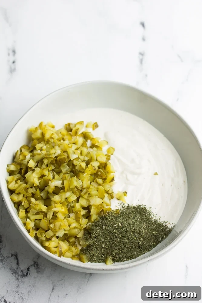 A vibrant bowl showcases the three foundational ingredients for vegan tartar sauce: creamy vegan mayo, finely diced dill pickles, and fresh, aromatic dill.