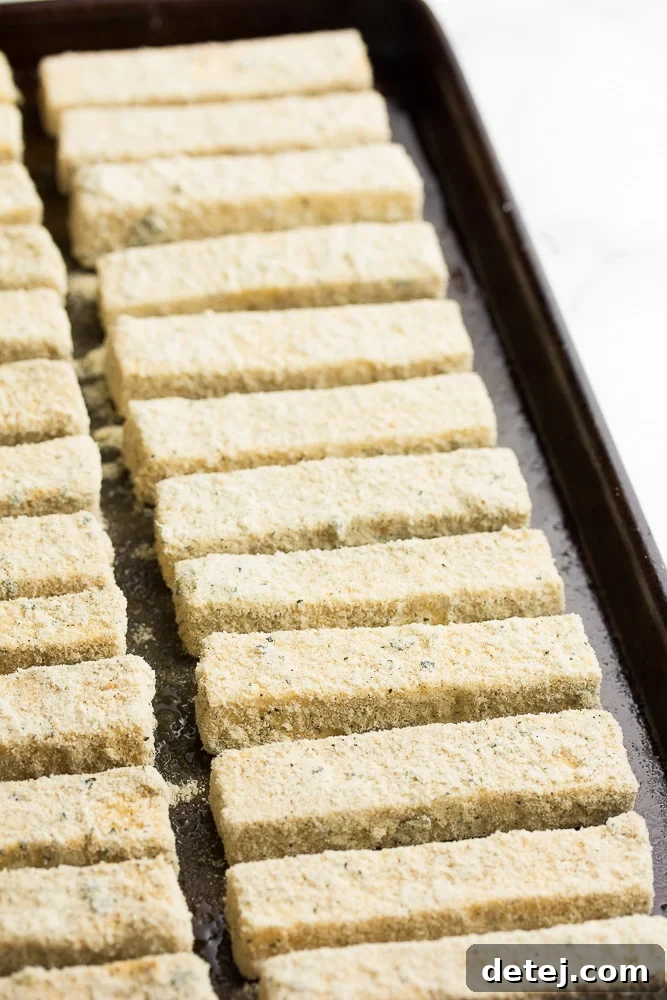 Several breadcrumb-coated tofu sticks arranged neatly on a baking sheet, ready for cooking.