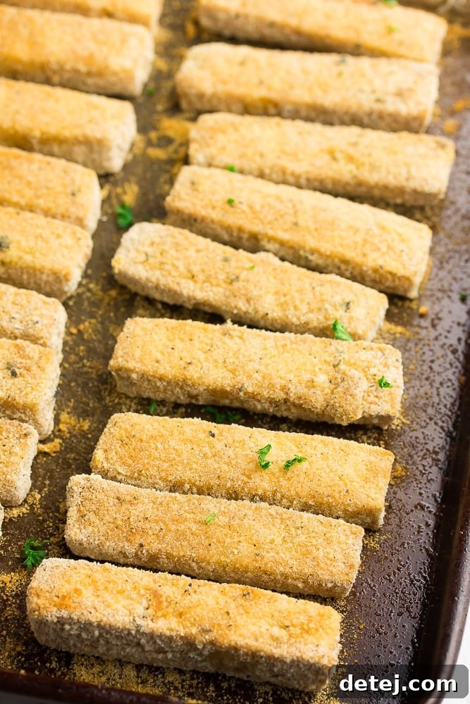 A batch of freshly baked, golden-brown tofu fish sticks cooling on a baking sheet, ready to be served.