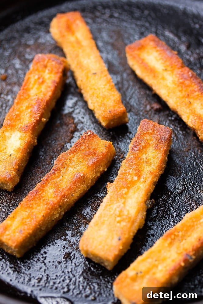 Golden-brown crispy tofu fish sticks cooking in a thin layer of oil in a cast-iron pan.