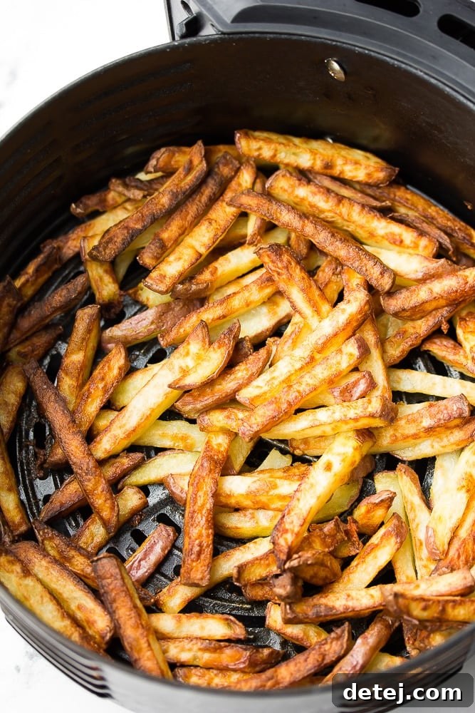 Crispy golden french fries piled high in an air fryer basket, garnished with fresh parsley.