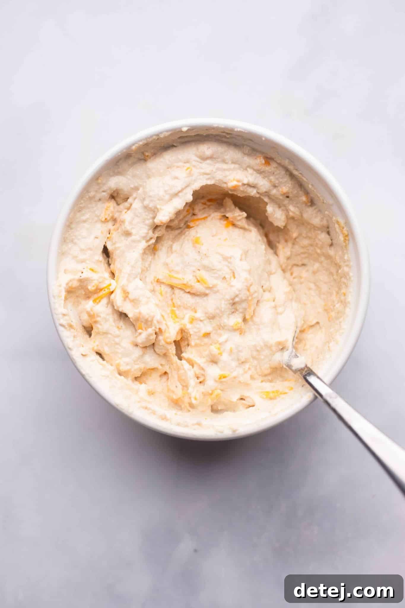 using a spoon to stir a vegan cream cheese mixture in a white bowl.