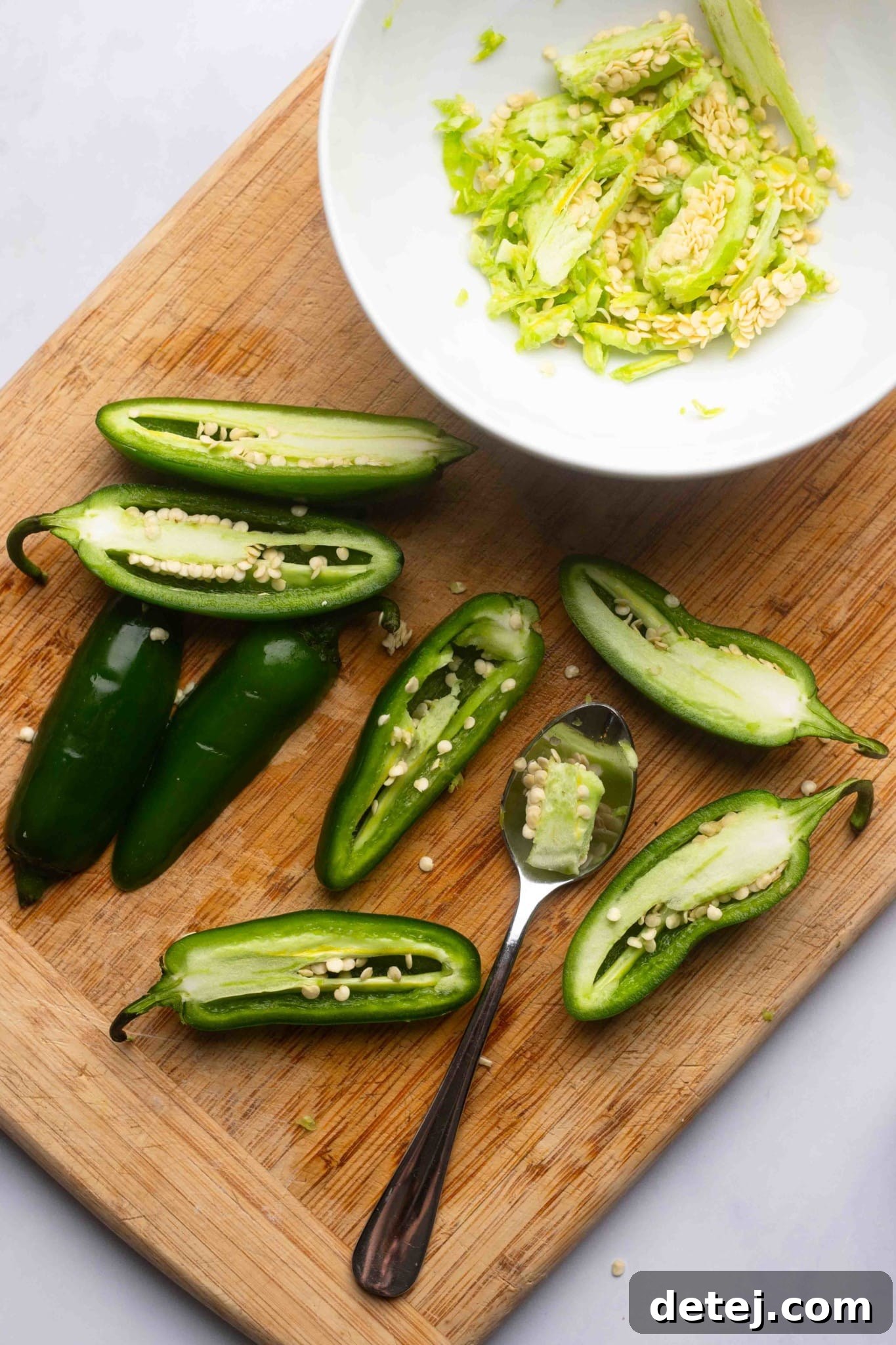 using a spoon to scrape the seeds out of halved jalapeno peppers.
