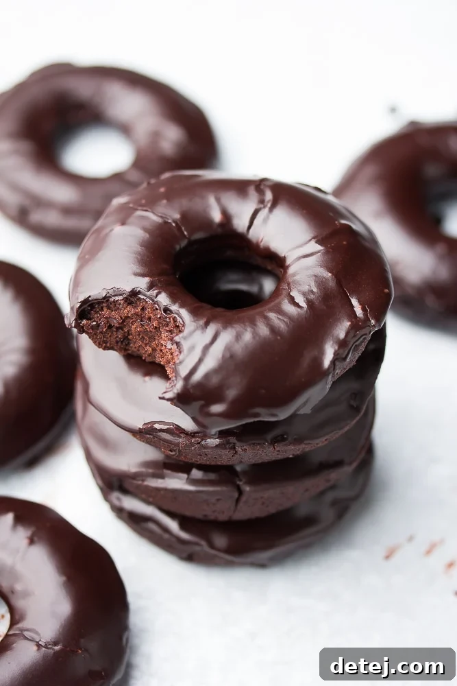 A charming stack of three baked vegan chocolate donuts, with the top donut enticingly revealing a bite taken out.
