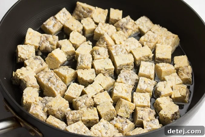 Tempeh cubes being steamed in water in a large skillet with a lid, preparing them for a delicious BBQ sauce coating.