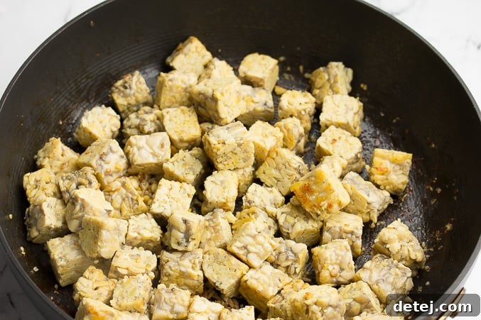 Crispy golden brown tempeh cubes frying in a skillet with olive oil, ready to be coated in barbecue sauce.