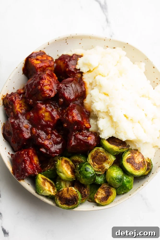 A beautifully arranged bowl featuring flavorful BBQ tempeh, creamy mashed potatoes, and perfectly roasted brussels sprouts, creating a wholesome and satisfying meal.