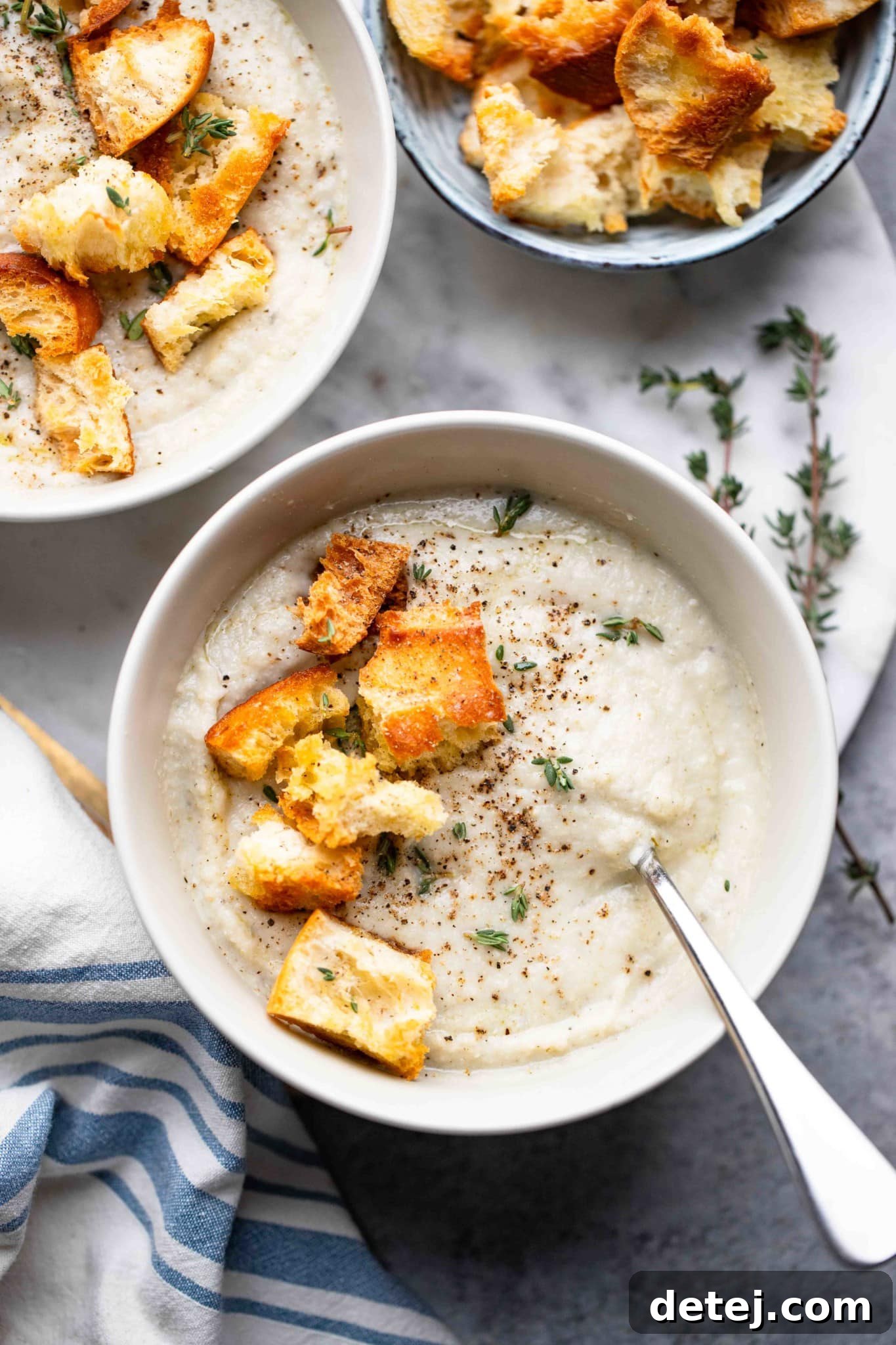 A steaming bowl of creamy vegan cauliflower soup, garnished with crispy croutons and fresh herbs, ready to be enjoyed.