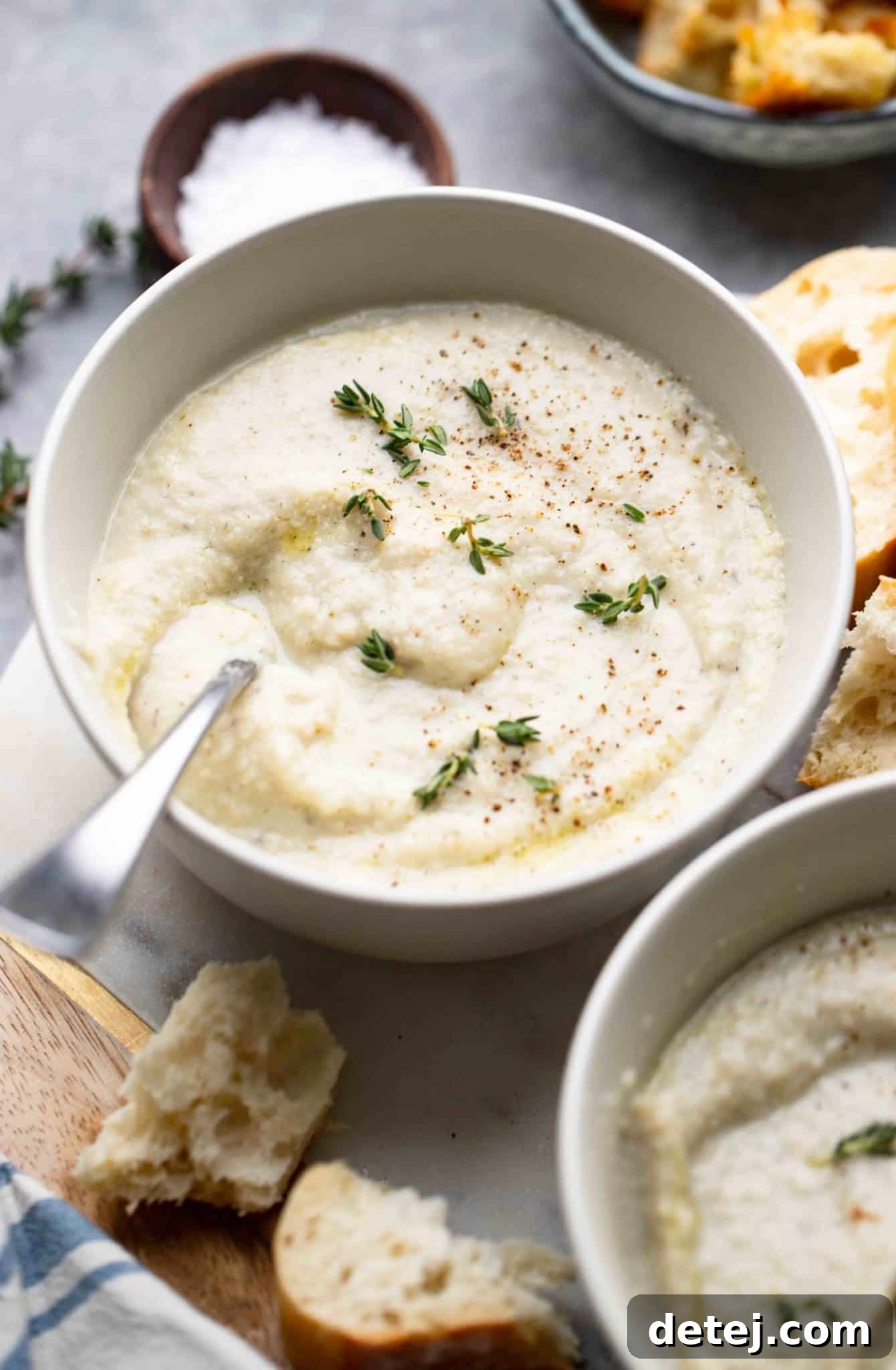 Another perspective of a bowl of creamy vegan cauliflower soup, elegantly topped with fresh herbs, emphasizing its inviting texture.