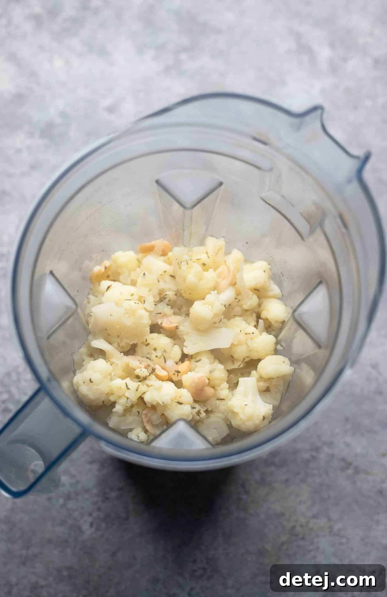 Hot cooked cauliflower soup ingredients carefully being spooned into a high-powered blender for puréeing.