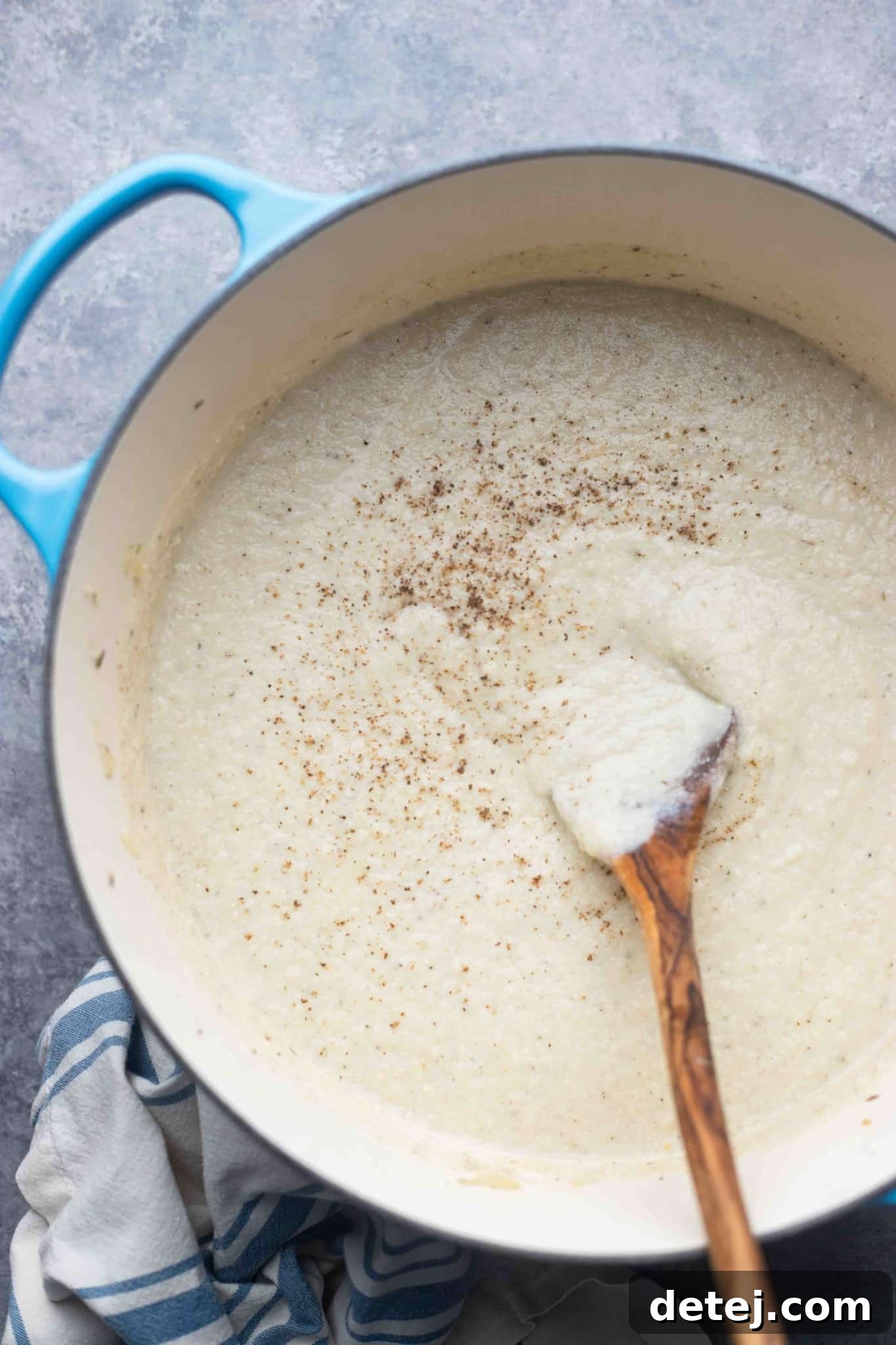 A wooden spoon stirs the perfectly smooth and creamy vegan cauliflower soup in a large pot, ready for serving.
