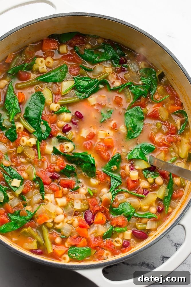 A large soup pot overflowing with vibrant, vegetable-packed vegan minestrone soup, garnished with fresh herbs.