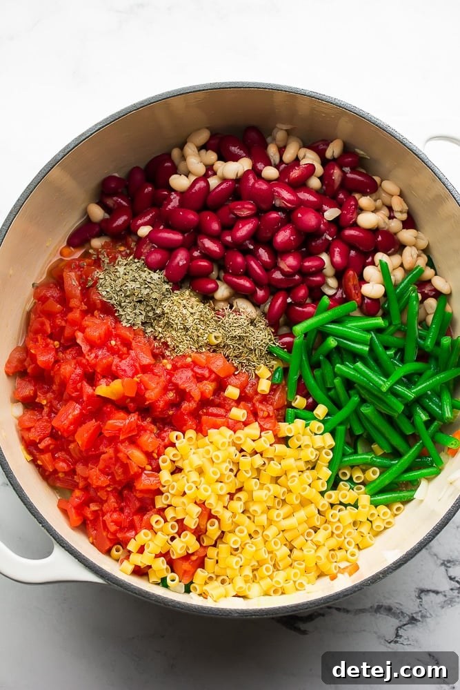 All the ingredients for vegan minestrone soup, fresh and vibrant, arranged around a large white pot.