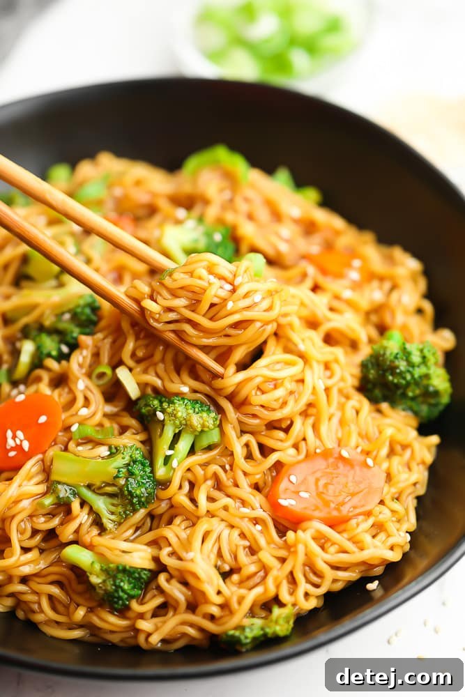 Chopsticks picking up a delectable bite of vegan teriyaki noodles from a beautifully presented bowl, highlighting the rich sauce and fresh vegetables.