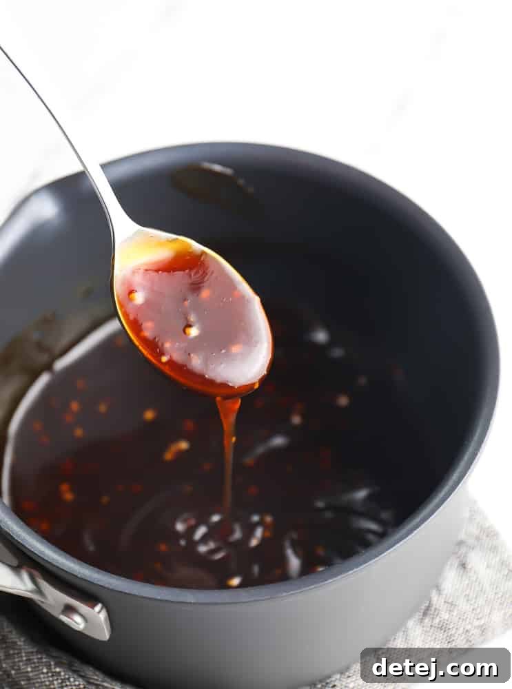 A metal spoon scooping a generous amount of dark, glossy teriyaki sauce from a black pot, showcasing its rich, thick consistency.