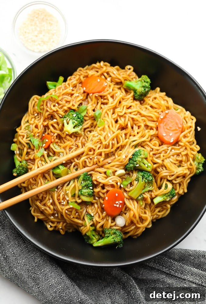 Overhead view of a black bowl filled with perfectly tossed teriyaki noodles and colorful vegetables, with chopsticks resting on the rim.