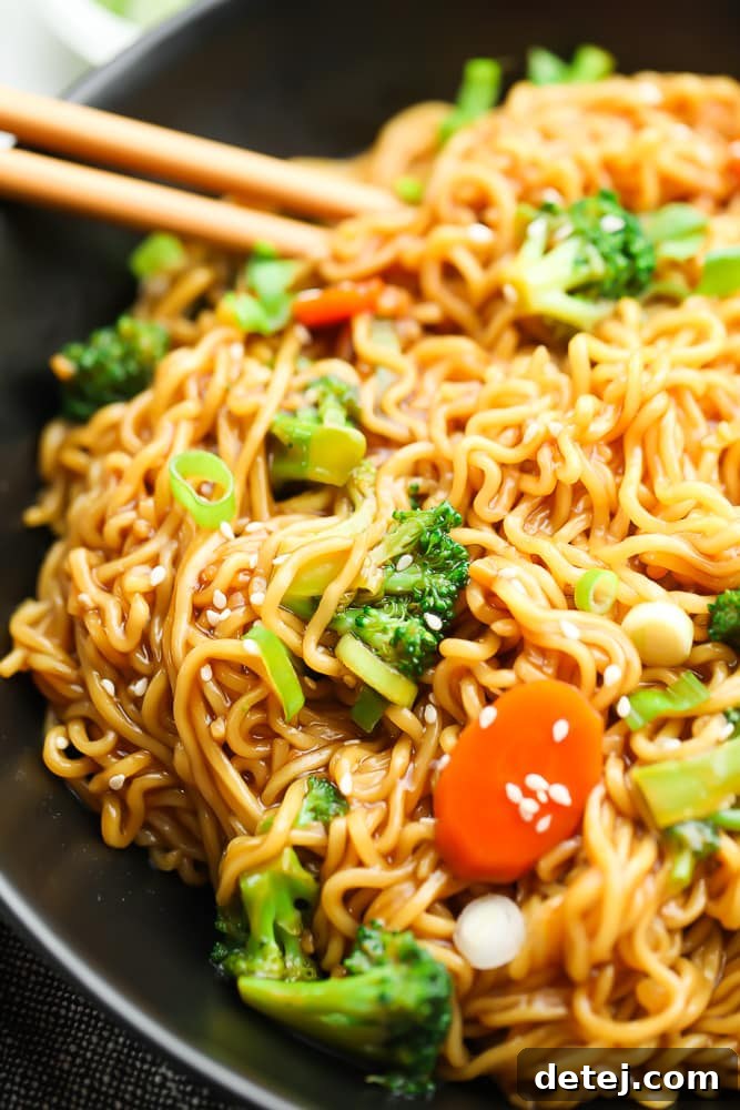 Close-up shot of saucy teriyaki noodles with visible vegetables in a black bowl, emphasizing the appealing texture and rich color.