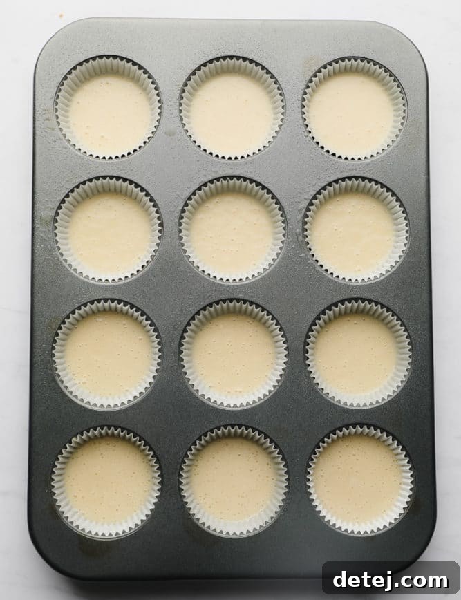 An unbaked tray of cupcakes in paper liners, filled with smooth, pale yellow batter, ready for the oven.