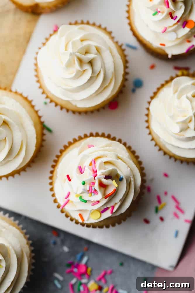 A bird's eye view of several frosted vegan vanilla cupcakes, some adorned with colorful sprinkles, others plain, showcasing their tempting appearance.