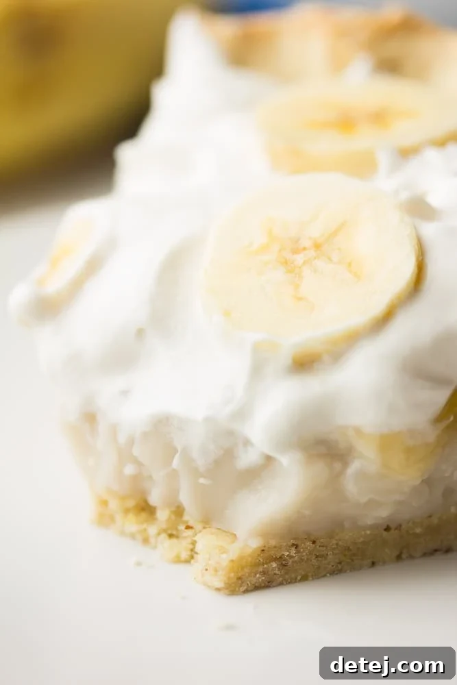 Close-up shot of the creamy Vegan Banana Cream Pie, highlighting the smooth texture of the custard and the neatly arranged banana slices beneath the whipped topping.