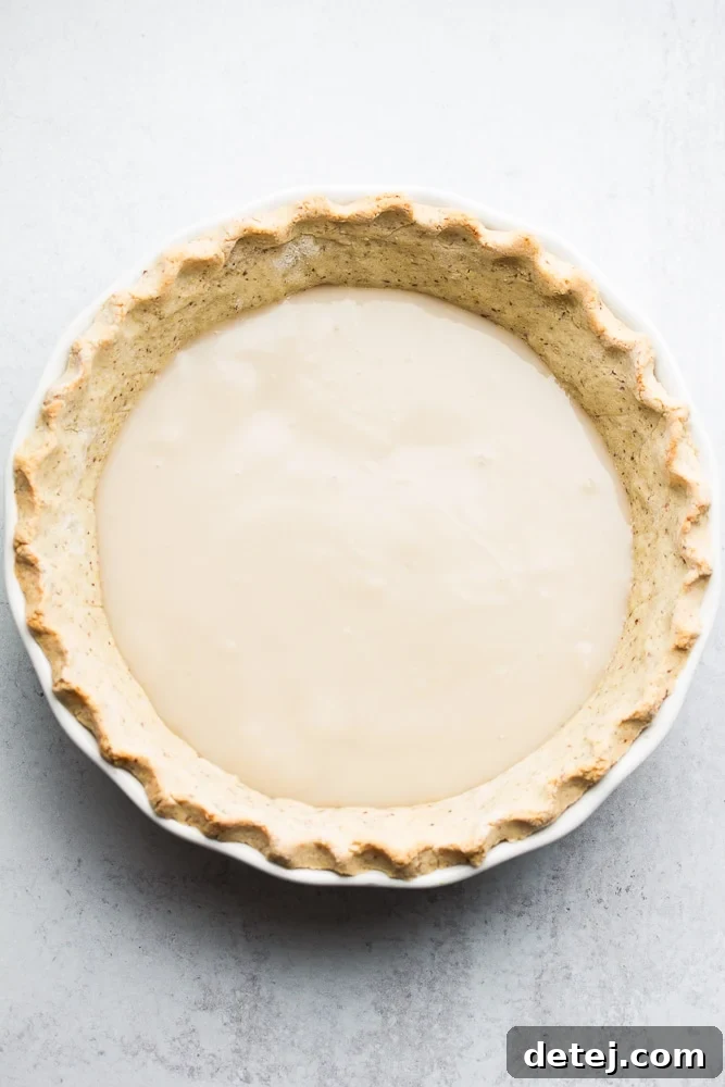 A golden, pre-baked pie crust filled with creamy, light-yellow vanilla custard, ready for chilling.
