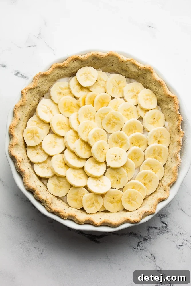 Sliced ripe bananas beautifully layered over the creamy vanilla custard in a pie crust, preparing for the final topping.