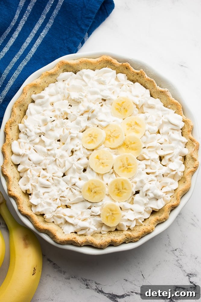 The finished Vegan Banana Cream Pie, topped with a generous swirl of fluffy vegan whipped cream and garnished with fresh banana slices.
