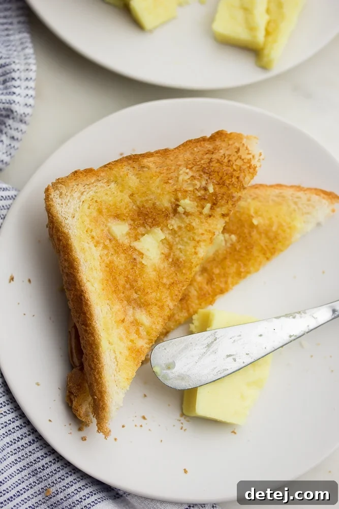A slice of white bread toast with melted vegan butter and a knife nearby
