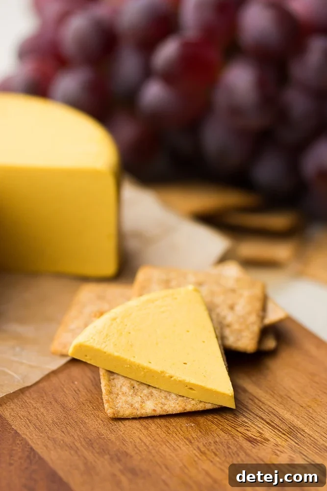 piece of sliced vegan cheddar on a cracker, garnished with a sprig of rosemary