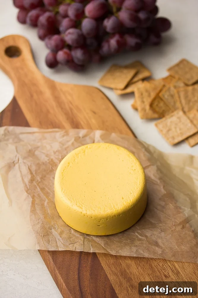 a block of homemade vegan cheddar cheese on a wooden board with crackers and grapes
