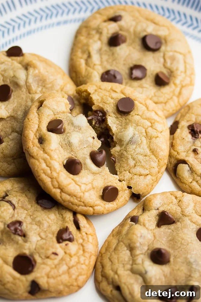 A delectable pile of vegan chocolate chip cookies, with the top cookie expertly split in half to reveal its soft, chewy interior filled with melted chocolate chips.