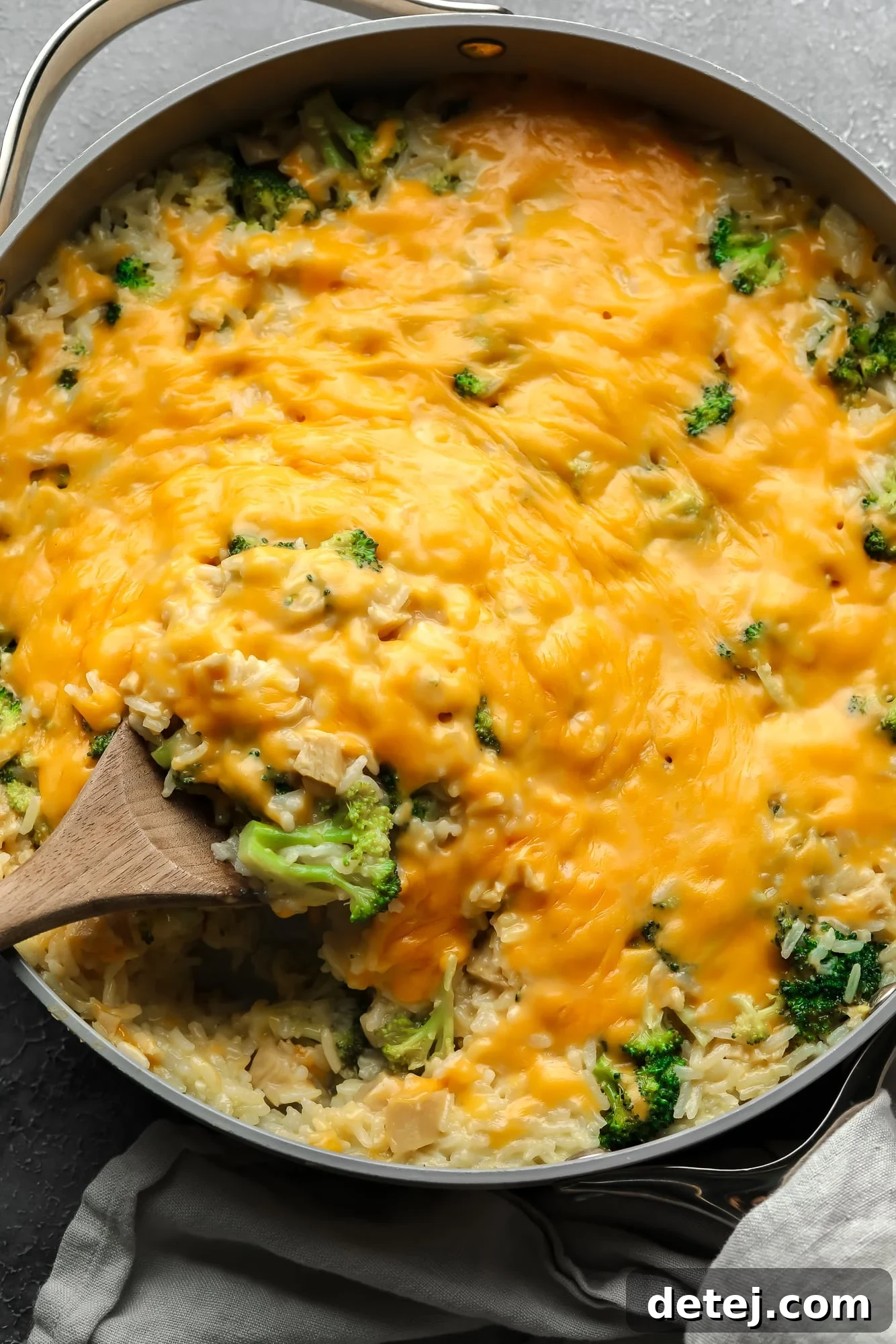 A wooden spoon serving a generous portion of cheesy vegan broccoli and rice casserole, highlighting the creamy texture and vibrant green broccoli.